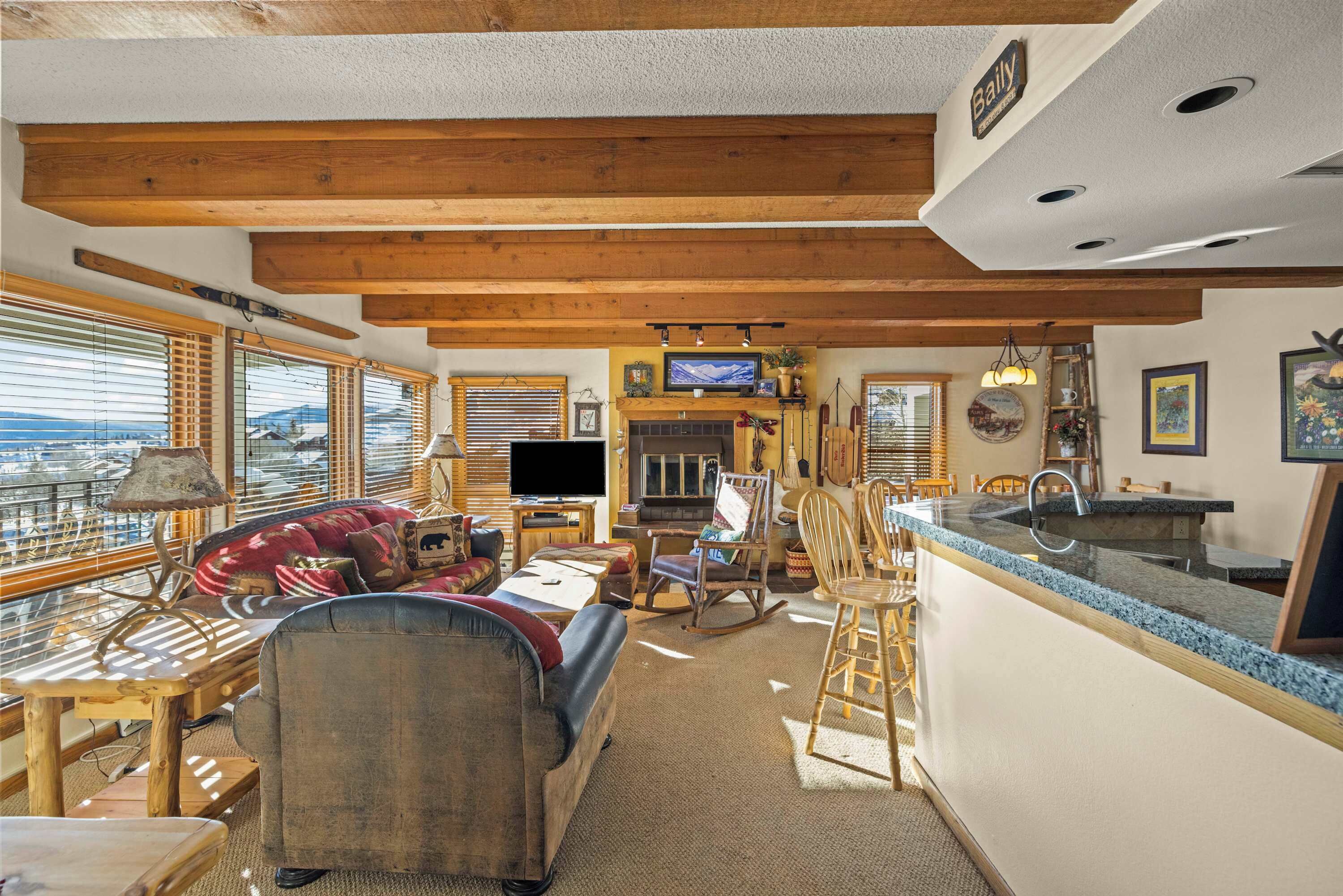 A cozy living room with a fireplace, wooden beams, a television, and a dining area with a bar counter.