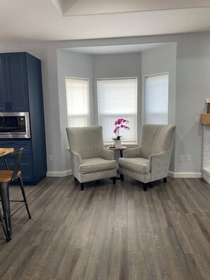 A modern living room with two armchairs, a small table, and a built-in microwave. - The Gathering at Jonmart SE Salem 5-bedroom house tranquil with AC, fenced Yard. (Salem)
