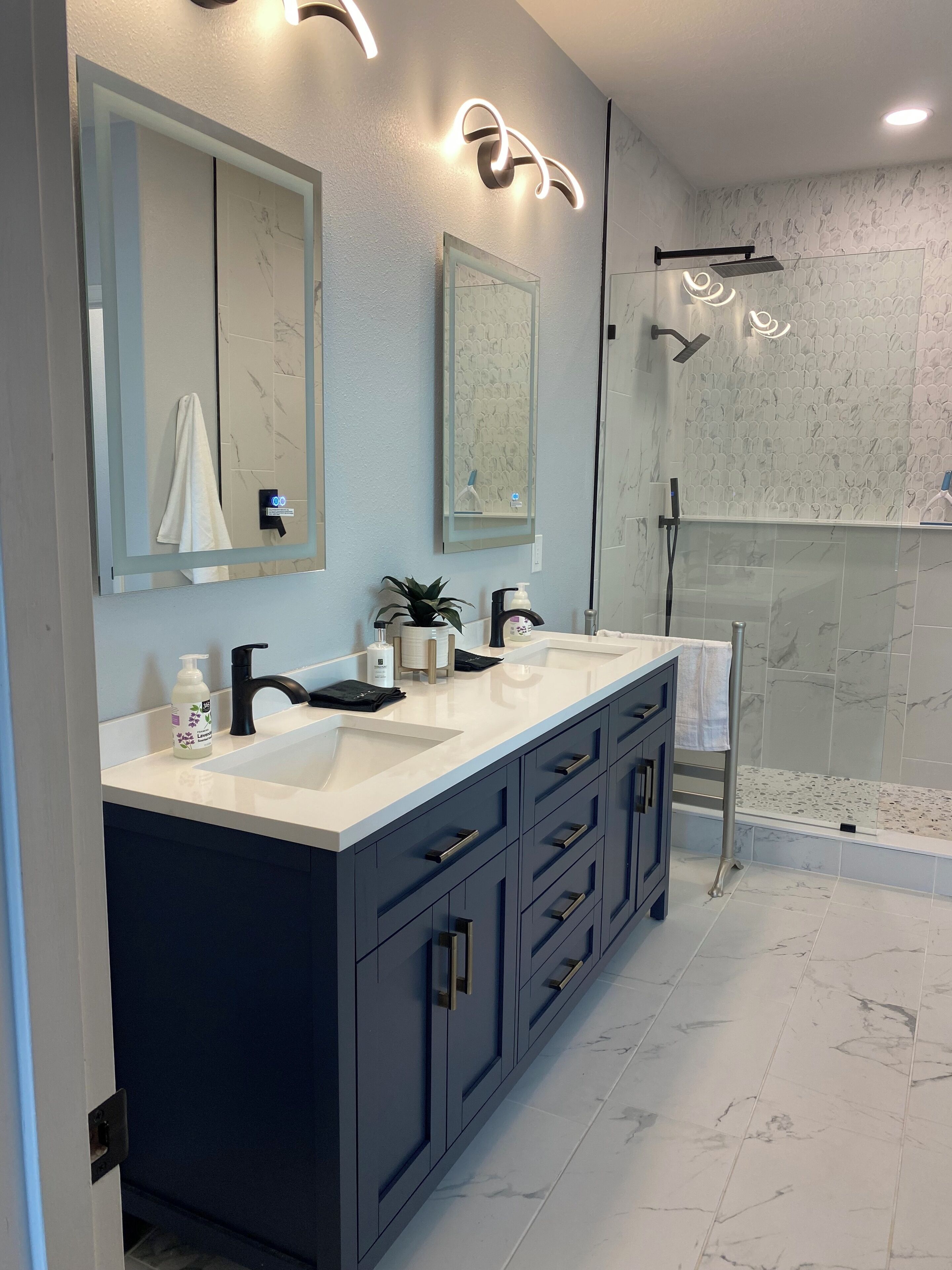 Un baño moderno con dos lavamanos, armarios oscuros y cabina de ducha de cristal.