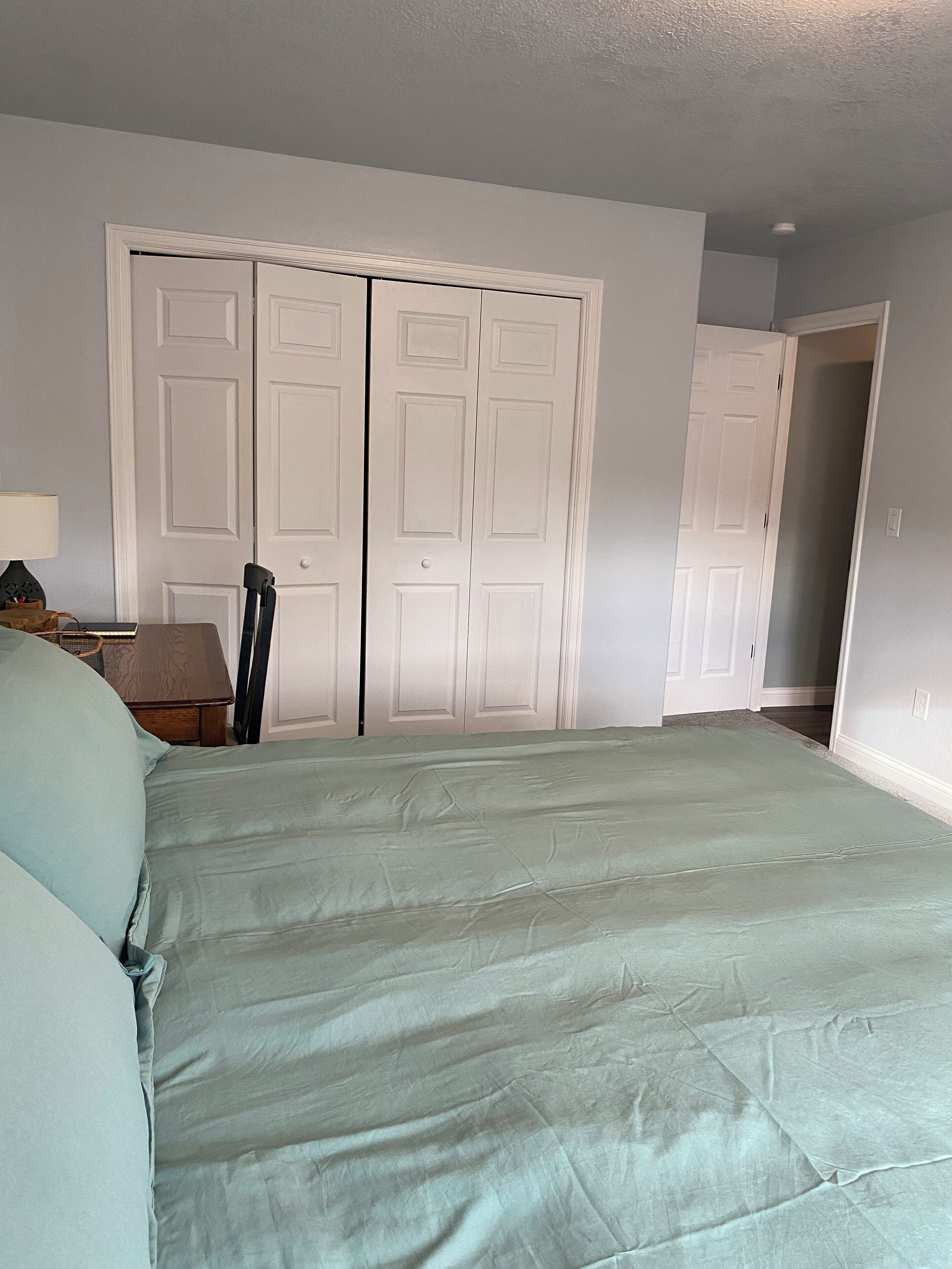 Un dormitorio con cama, mesita de noche, lámpara y dos puertas blancas.