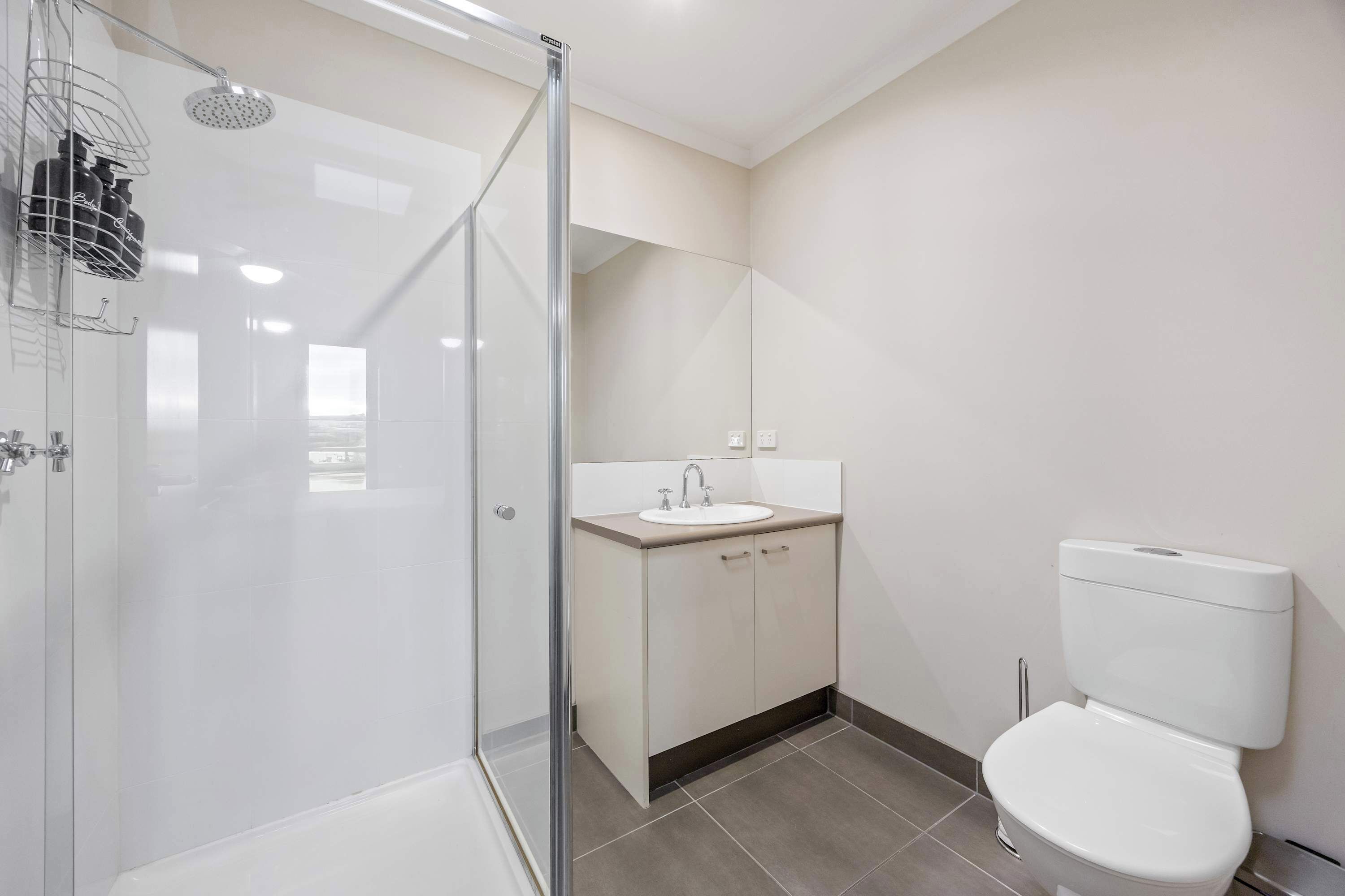 Een moderne badkamer met een douche met glazen wand, een wastafel met spiegel erboven en een toilet.