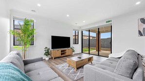 Ein modernes Wohnzimmer mit grauen Sofas, einem Holztisch, einem Fernseher und einer großen Schiebeglas-Haustür.