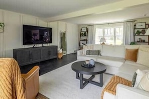 A modern living room with a large flat-screen TV, a sofa, a coffee table, and a bookshelf.