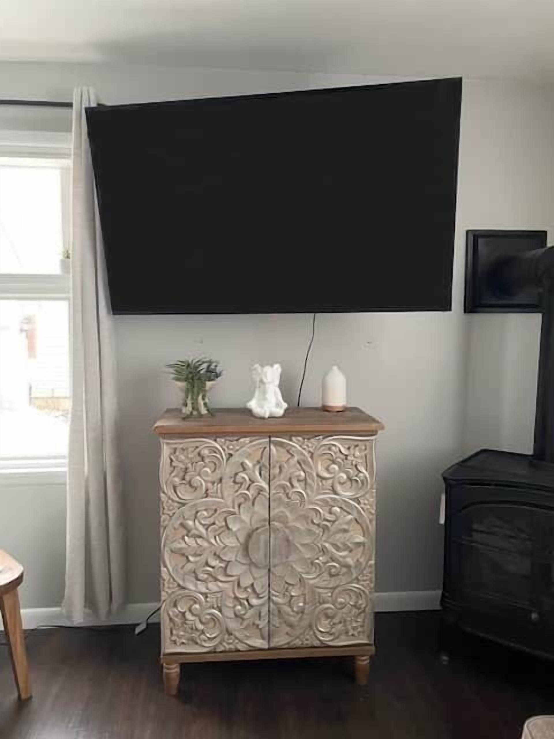 A room with a large flat-screen TV mounted on the wall, a decorative cabinet with intricate carvings, and a black fireplace.