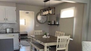 A dining area with a wooden table and chairs, a clock on the wall, and a kitchen in the background. - LVR's 3 Sister's Cape (Lewiston)