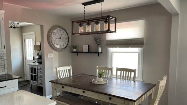 A dining area with a wooden table, white chairs, and a hanging light fixture. - LVR's 3 Sister's Cape (Lewiston)