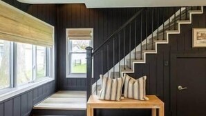 Un interior moderno con una escalera de madera oscura, un banco de madera con cojines y un ventanal con vistas al exterior.