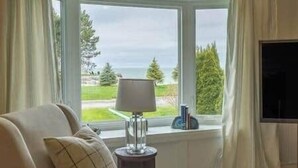 Una habitación con vista al mar, una lámpara en una mesita auxiliar y un televisor a la derecha.