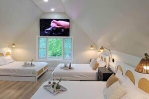 Une chambre avec deux lits, une grande fenêtre donnant sur un paysage verdoyant et un téléviseur fixé au mur.