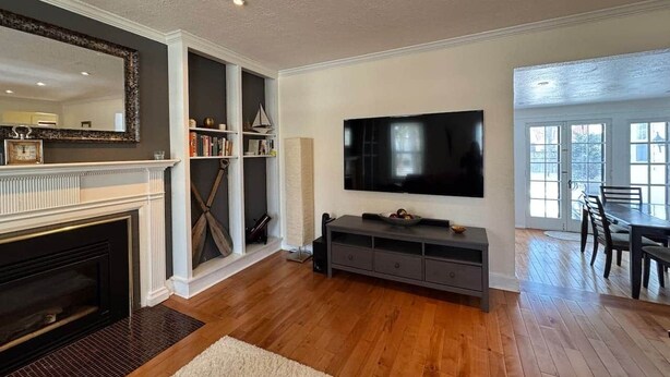 A living room with a fireplace, a television, a bookshelf, and a dining area with a table and chairs.