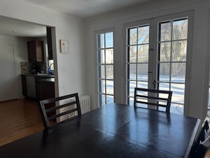 Un comedor con una mesa y sillas de madera oscura, una cocina al fondo y ventanas amplias con vistas a un paisaje nevado.