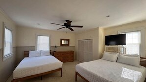 A bedroom with two single beds, a ceiling fan, a dresser, a TV, and a wardrobe.
