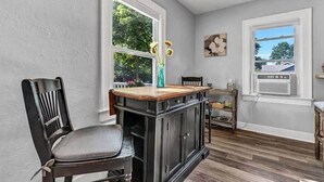 A room with a wooden floor, a dark wooden cabinet, a chair, a small table, and a window with a view of trees. - LVR - The Yellow House on 3rd (Lewiston)