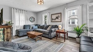 A living room with a sectional sofa, a coffee table, a side table with a lamp, and a patterned rug. - LVR - The Yellow House on 3rd (Lewiston)