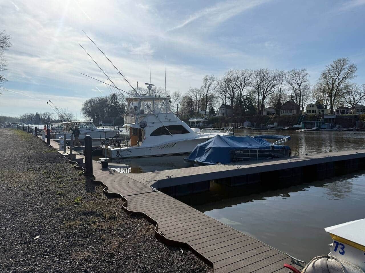 Un port de plaisance avec un bateau amarré, une passerelle en bois et une rangée de maisons en arrière-plan.