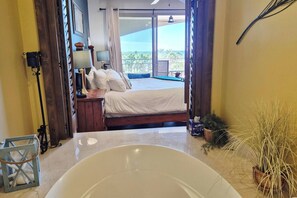 A bedroom with a large bed, a nightstand, a lamp, and a view of the balcony. - Elevated Bella Sirena Views: 2nd Floor Luxury (Puerto Peñasco)