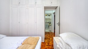Ένα υπνοδωμάτιο με δύο κρεβάτια, μια ντουλάπα και μια κουζίνα που φαίνεται μέσα από μια ανοιχτή πόρτα.