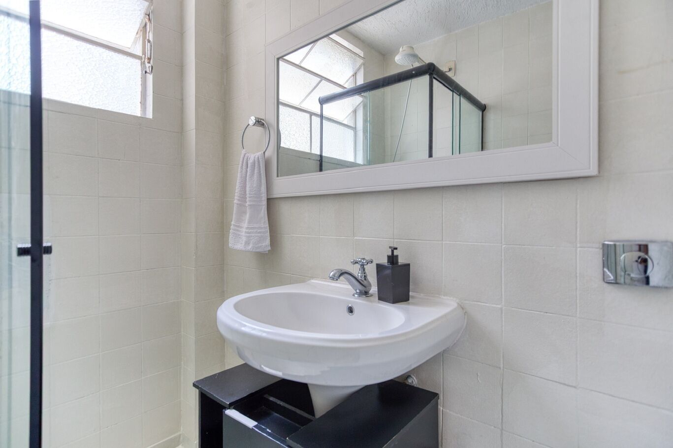 Une salle de bain avec un lavabo blanc, un miroir et une serviette suspendue à un anneau en métal.