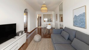 A modern living room with a flat-screen TV, grey sofa, and a dining area with a white table and chairs. - Pérola do Mar - Atlantic Escape (Caldas da Rainha)