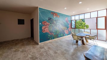 Una habitación con un mural grande, una zona de comedor con sillas y vista a espacios verdes afuera.