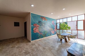 A room with a large mural, a dining area with chairs, and a view of greenery outside. - Hotel Santa Cruz Mazunte (Mazunte)