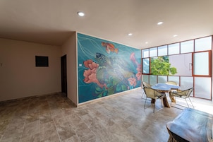 Una habitación con un mural grande, una zona de comedor con sillas y vista a espacios verdes afuera.