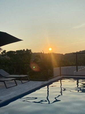 A swimming pool with a sun setting in the background, surrounded by greenery and a clear sky. - Hotel Santa Cruz Mazunte  (Mazunte)