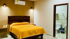 Ein Schlafzimmer mit einem Bett, einer Klimaanlage, einem Nachttisch und einem durch eine offene Tür einsehbaren Badezimmer.