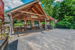 Een houten hut met een overdekte veranda, een bord waarop 'Stone Creek' staat, en een parkeerplaats met grind.