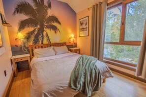 A bedroom with a bed, a nightstand, a lamp, a window with curtains, and a wall mural. - Pocono Riverfront House \ Outdoor Pool \ Sauna \ Hot tub (Pocono Township)