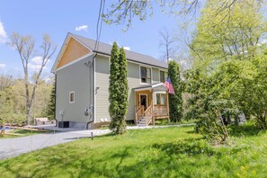 A two-story house with a porch, a small deck, and a front yard. - Pocono Riverfront House \ Outdoor Pool \ Sauna \ Hot tub (Pocono Township)