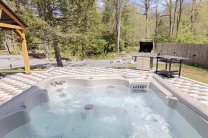 A hot tub with a wooden pergola, a barbecue grill, and a checkered patio. - Pocono Riverfront House \ Outdoor Pool \ Sauna \ Hot tub (Pocono Township)