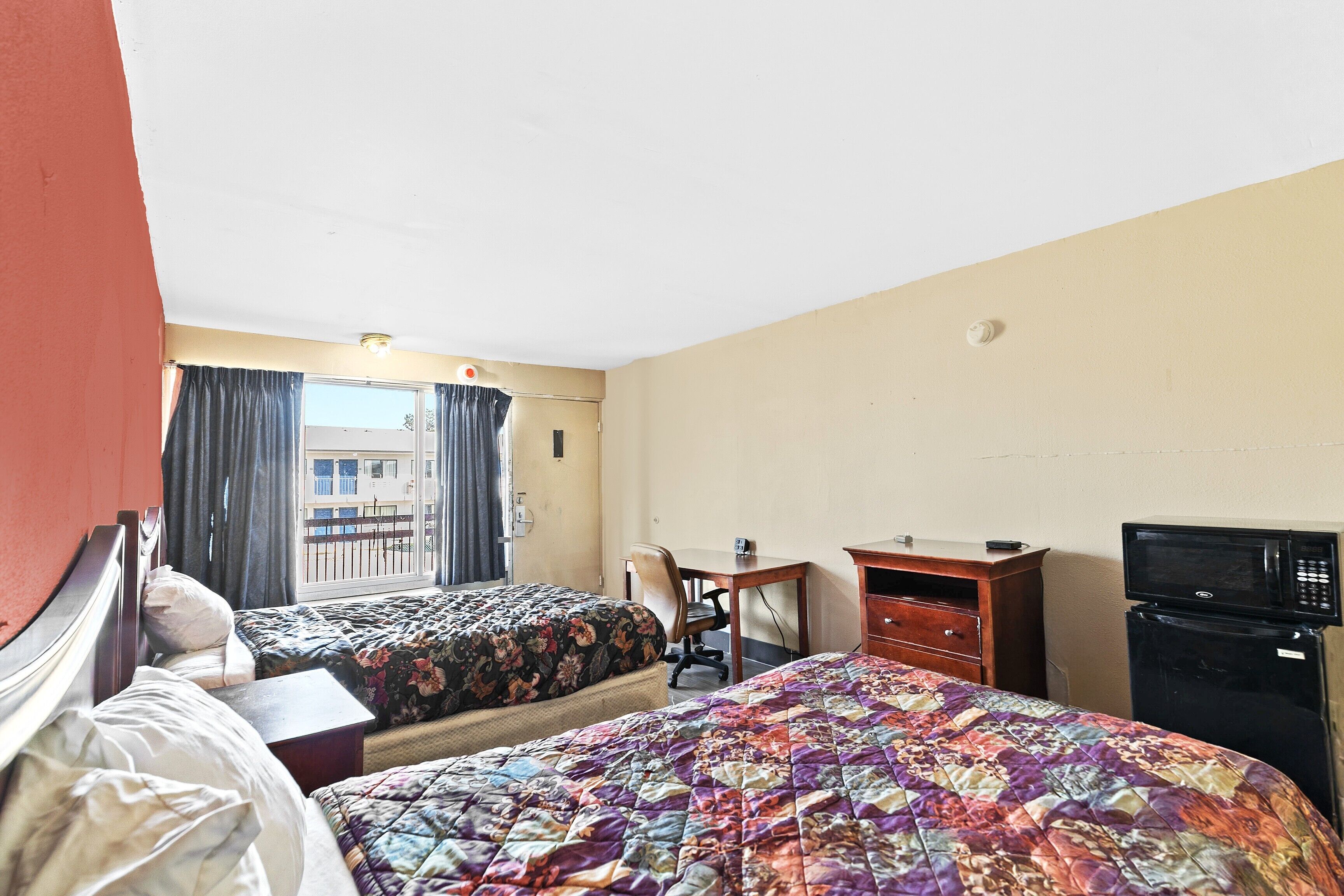 A hotel room with two beds, a desk, a chair, a television, and a window with curtains.