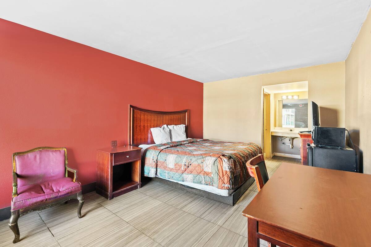 Une chambre d’hôtel comprenant un lit, une table de chevet en bois, une chaise, un bureau et un téléviseur.
