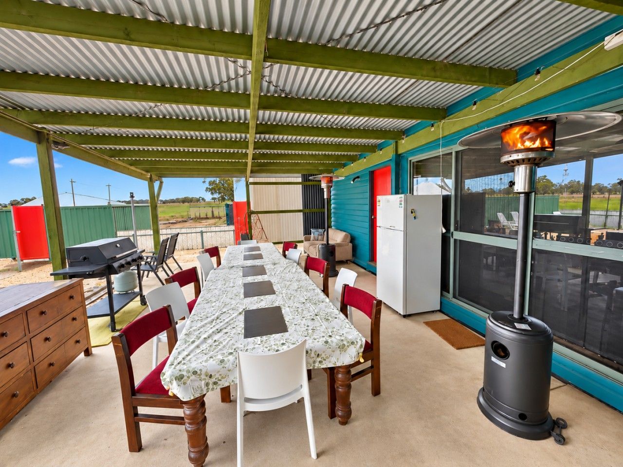 Un espace de restauration extérieur abrité, avec une longue table, des chaises, un barbecue et un poêle à bois.