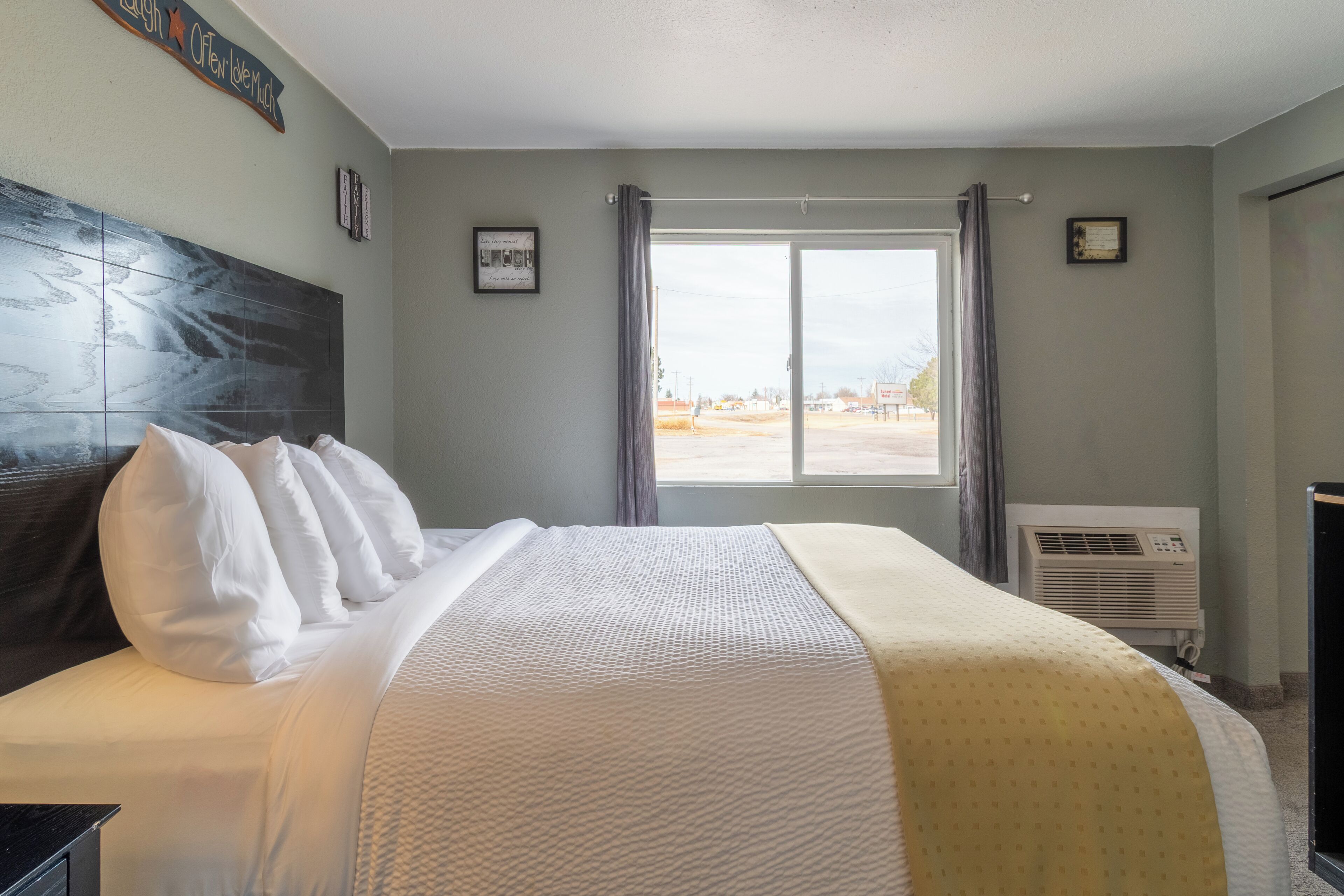 Una habitación de hotel con una cama grande, una ventana con cortinas, un aire acondicionado instalado en la pared y un cuadro enmarcado.