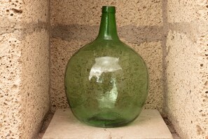 En grøn glasflaske med small hals, placeret på en stenhylde op ad en muret væg.