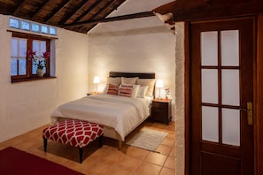 Ein Schlafzimmer mit einem Bett, Nachttischen, einer Holztür und einem Fenster mit Blumen.