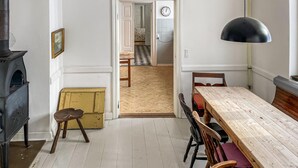 En matplats med ett träbord och stolar, en svart hänglampa, en gammal spishäll och en dörr som leder till en hall med ett mönstrat golv.