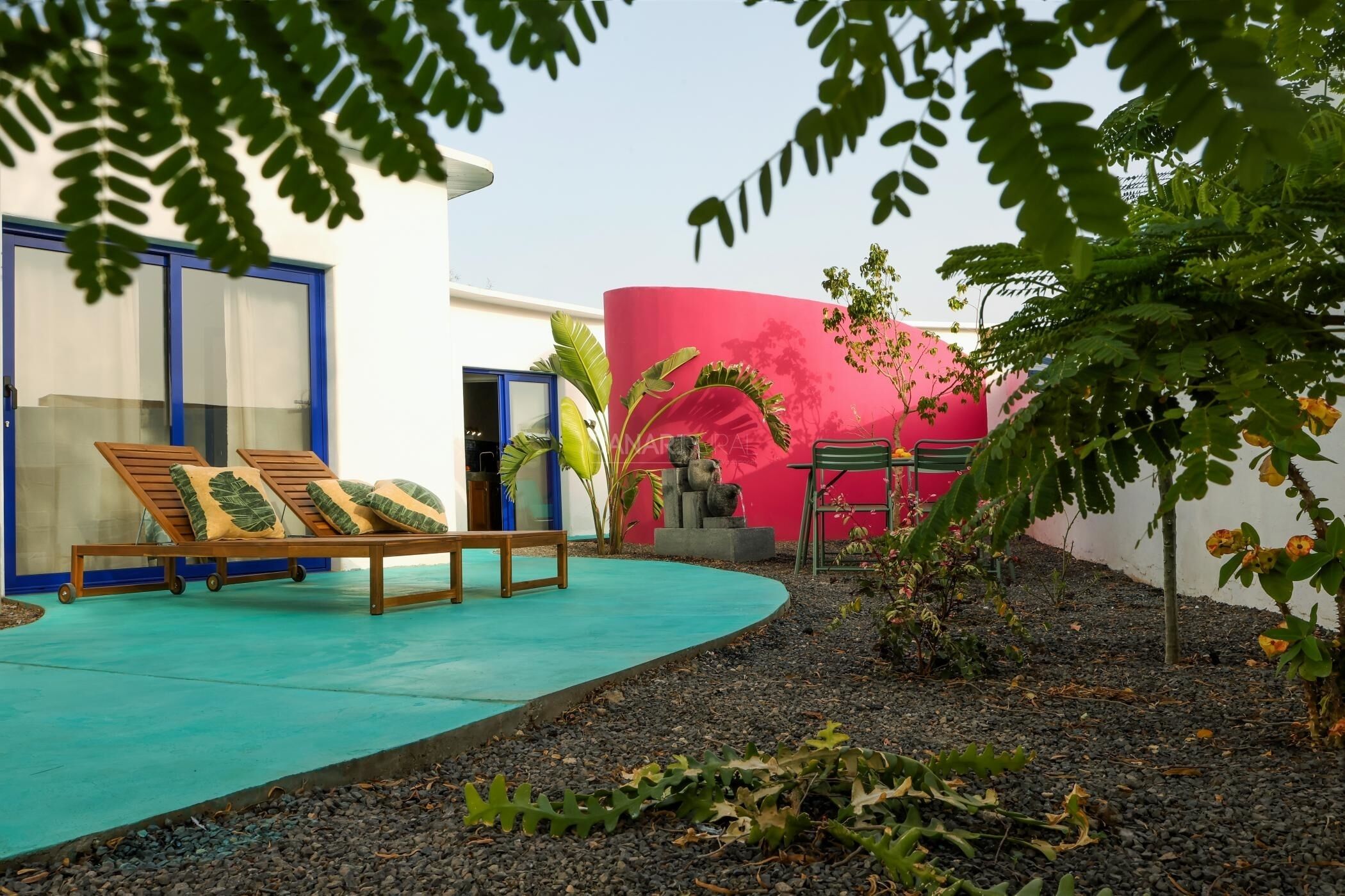 A pool area with lounge chairs, a pink wall, and a small garden.