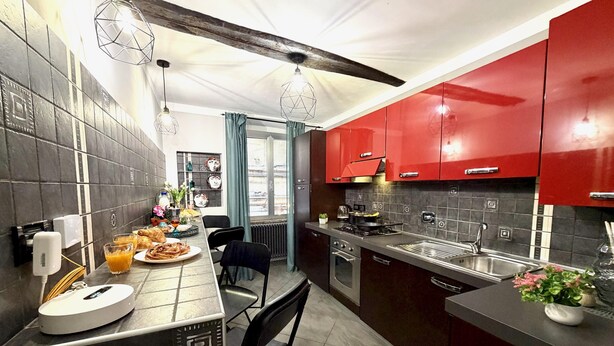 A modern kitchen with red cabinets, a dining area with a table set for breakfast, and a view of the outdoors through a window. - DIMORA DI PRE   ACQUARIO   GENOVABB.IT (GENOVA)