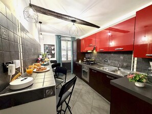 Una cocina moderna con armarios rojos, un comedor con mesa dispuesta para el desayuno y vistas al exterior a través de una ventana.