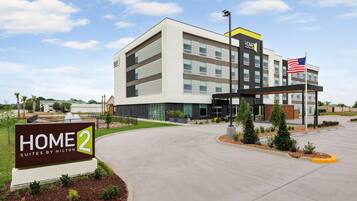 Un hôtel moderne, reconnaissable à son enseigne « HOME 2 Suites by Hilton » et à la présence d’un drapeau américain.