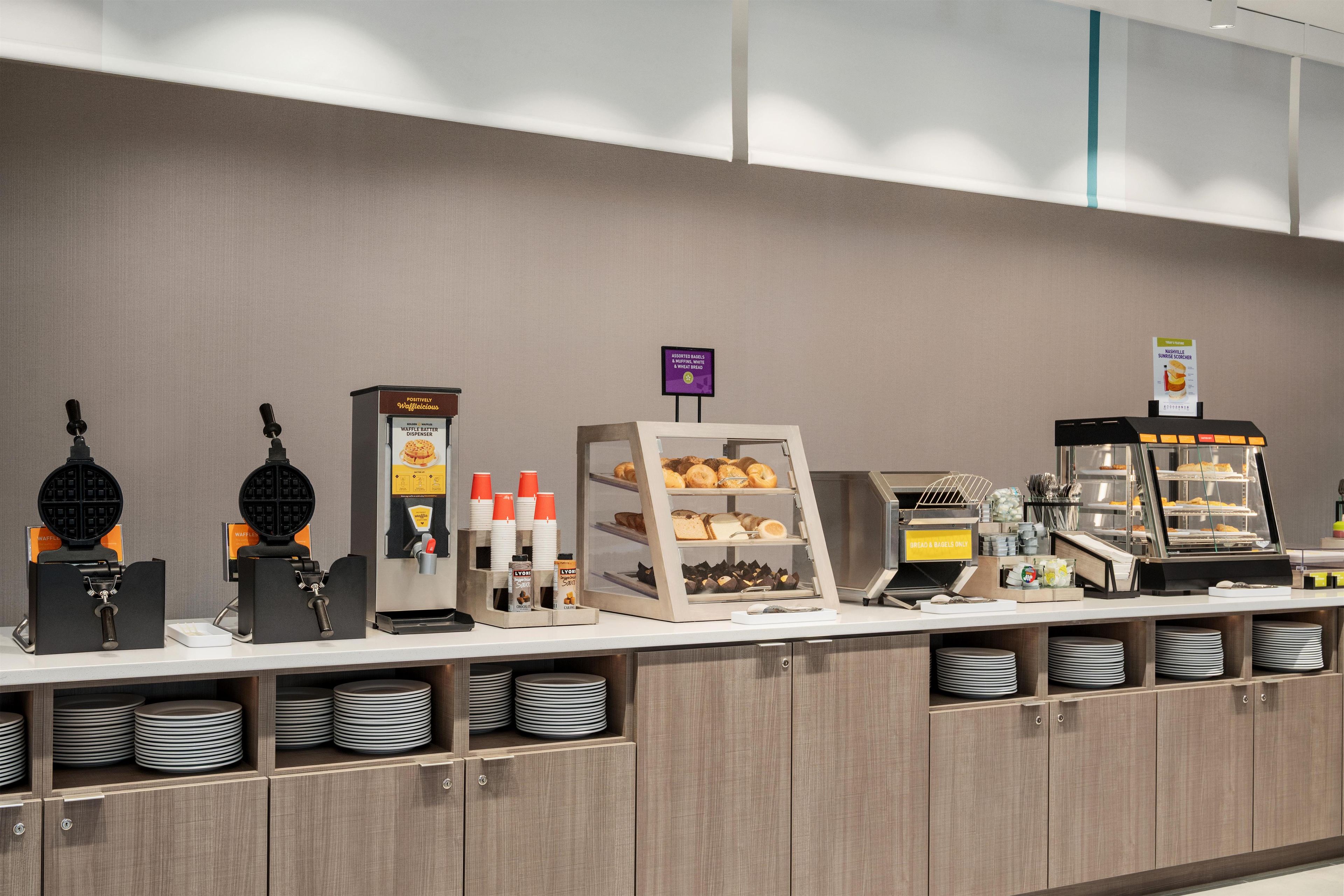Un bufé de desayuno con máquinas para hacer gofres, dispensadores de café y una variedad de pasteles.