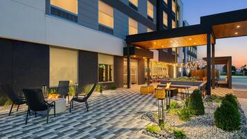 Un espace extérieur moderne aménagé avec un foyer, des chaises et un patio couvert.