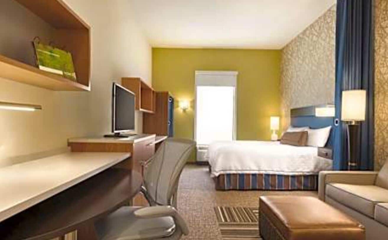 A hotel room with a bed, a desk, a chair, a TV, and a sofa.