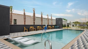 Piscina com espreguiçadeiras, um pequeno edifício e palmeiras.