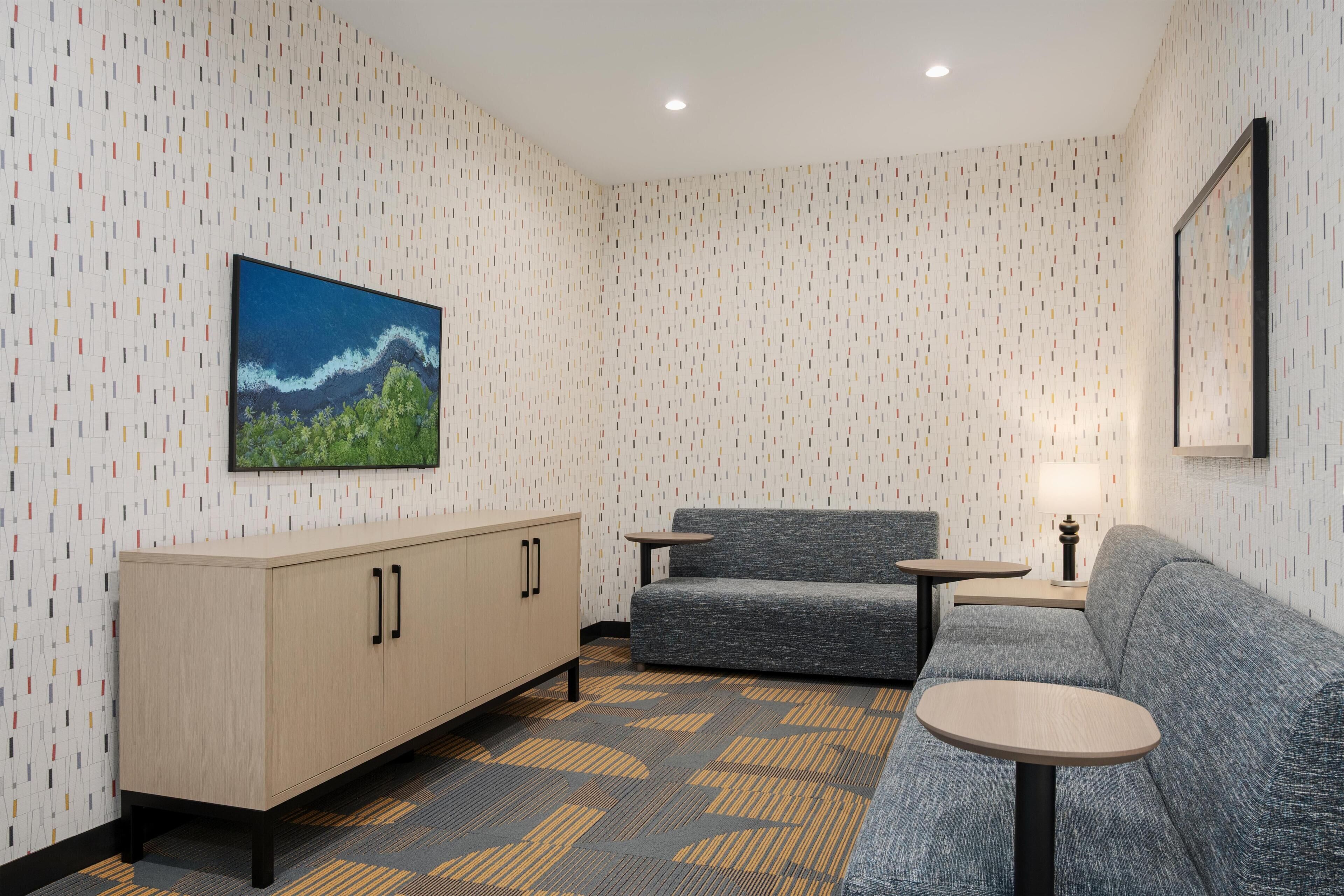 Quarto moderno com papel de parede estampado, um sofá, uma mesinha, um armário e um quadro na parede.