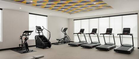 Un gimnasio con cintas de correr, elíptica y banca.