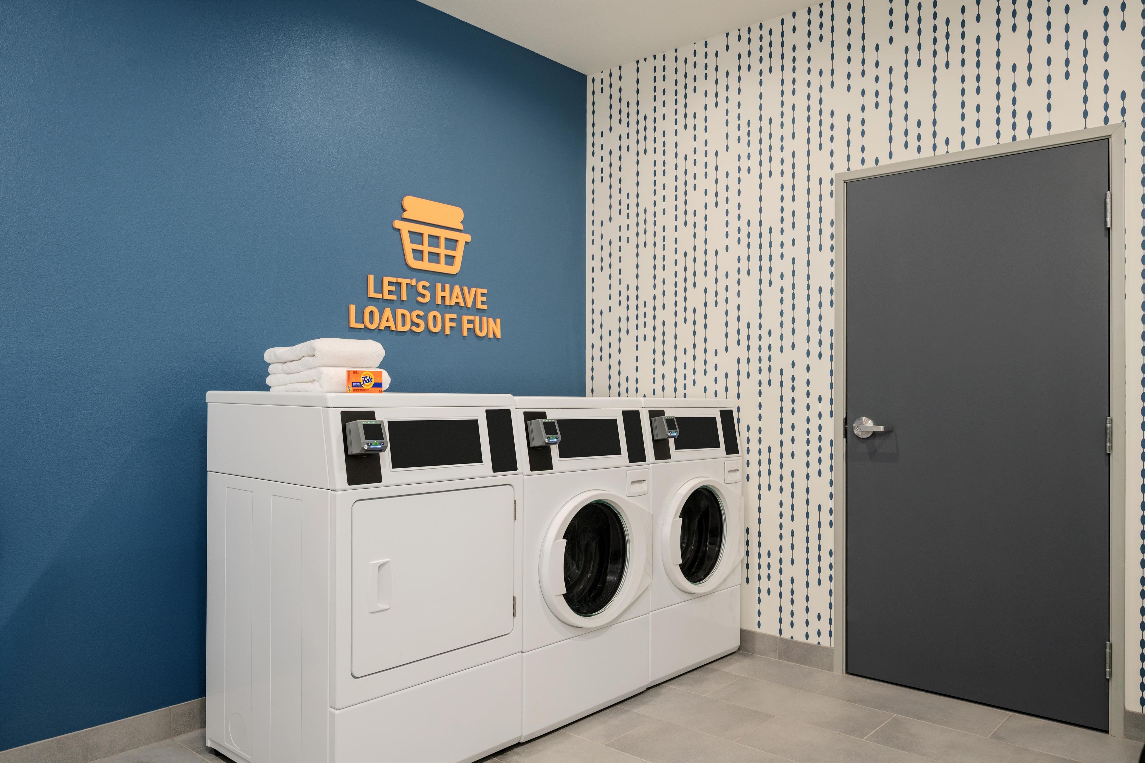 Un espace buanderie comprenant un lave-linge et un sèche-linge fixés au mur, une porte et un mur orné d’une citation inspirante.